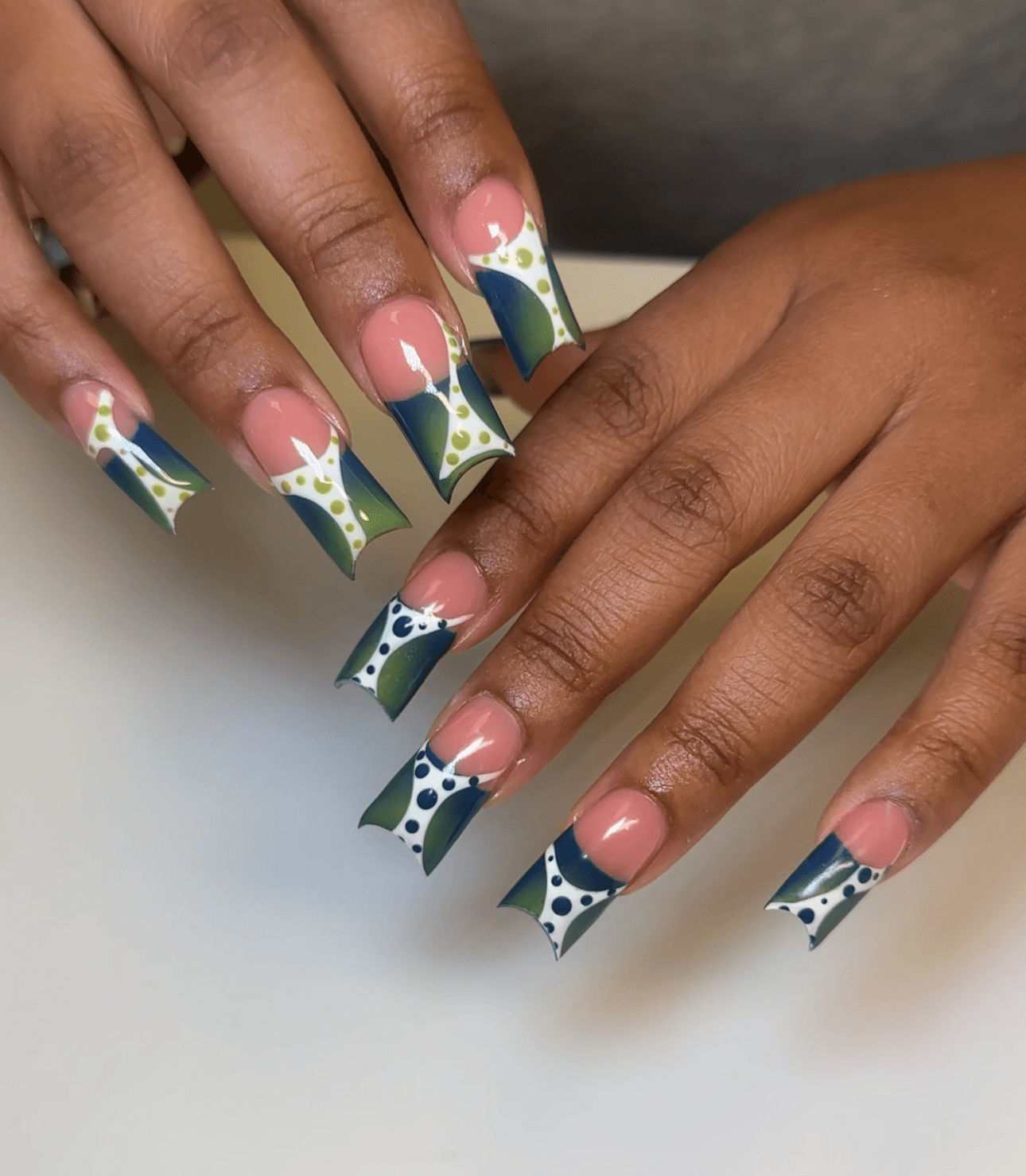 Hands with decorated nails featuring floral and abstract patterns in green, white, pink, and blue colors.