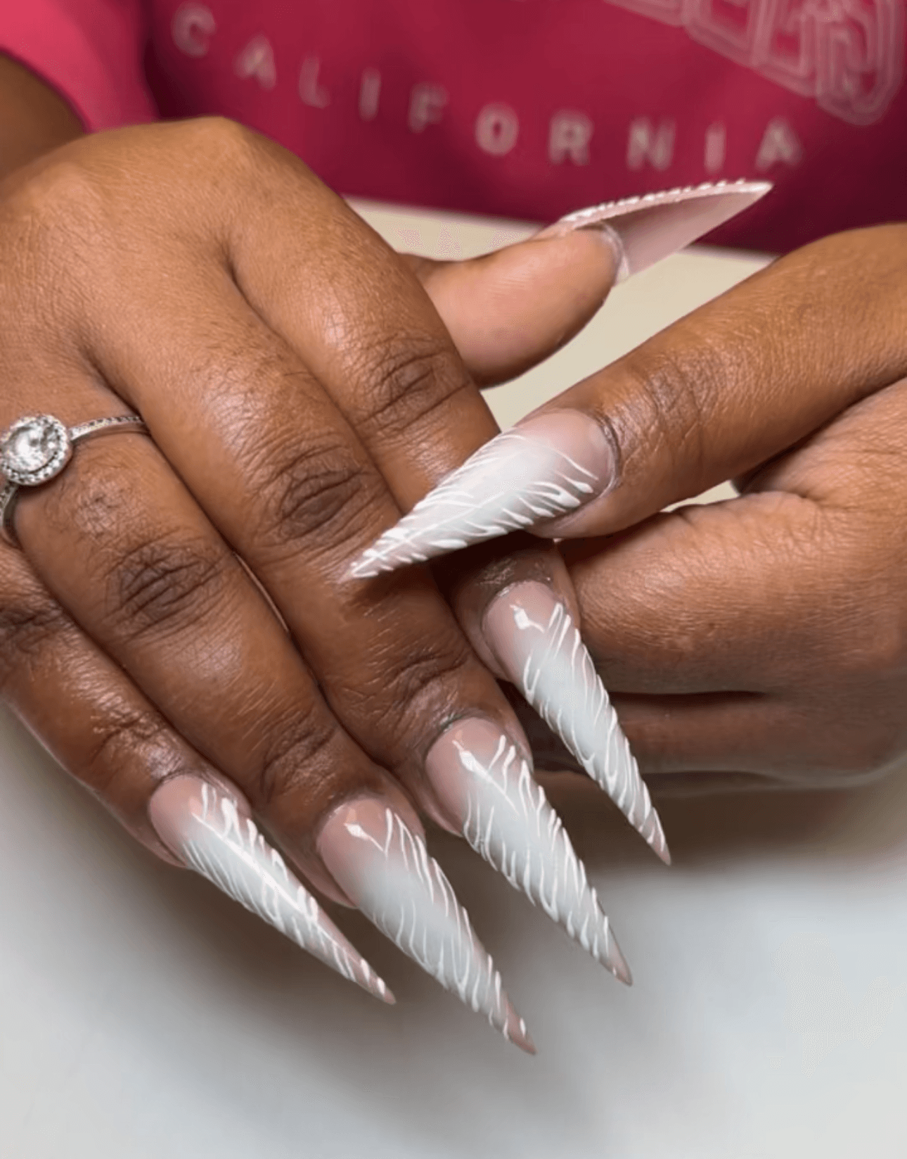 Close-up of hands with long, pointed, white acrylic nails and a ring on the finger.