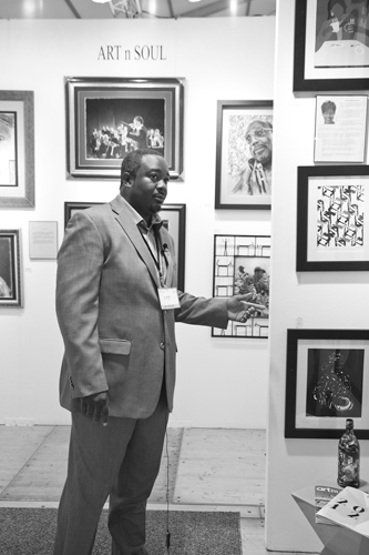 Man in suit standing in art gallery, looking at framed artwork on wall, with gallery labels visible.