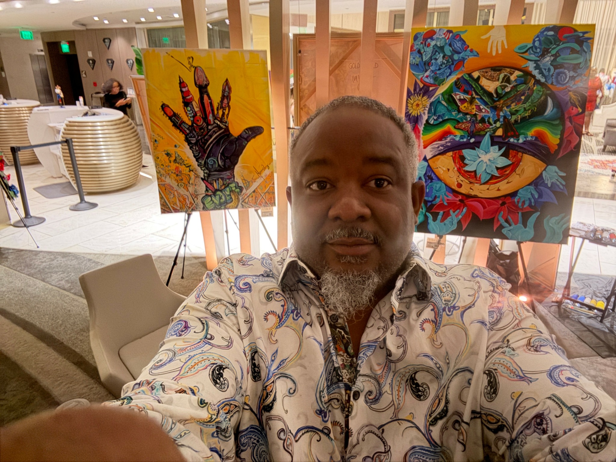 Man taking selfie in art gallery with colorful paintings behind him.