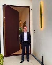Man in suit standing in doorway with open door, wall with yellow light fixture on right side.