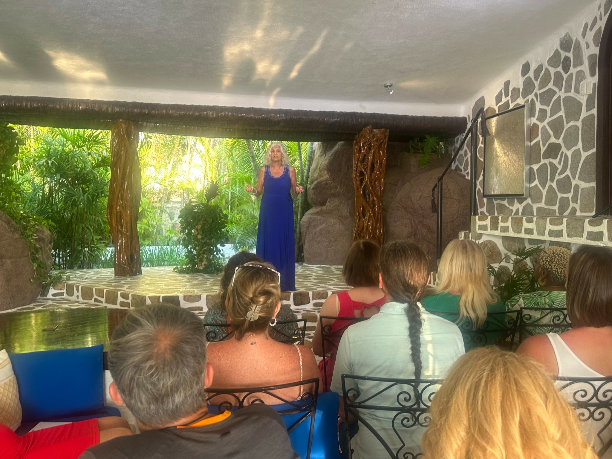 Person in blue dress performing on an outdoor stage with audience seated in front.