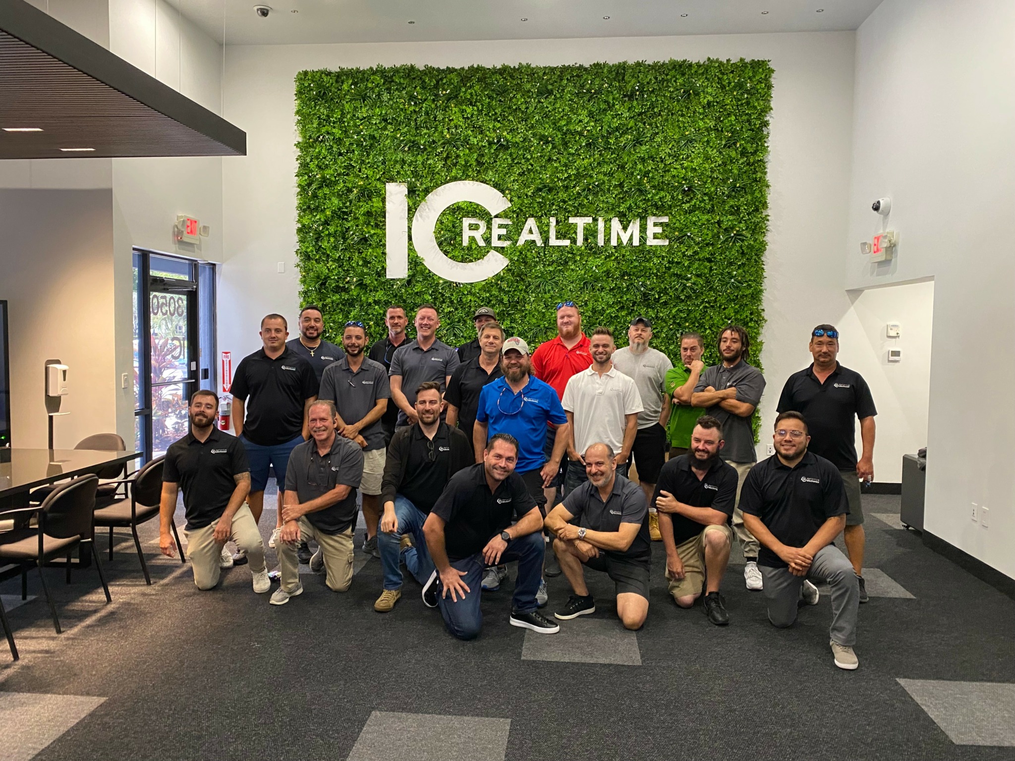Group of 20 people posing indoors in front of a green wall with 'IC REALTIME' logo.