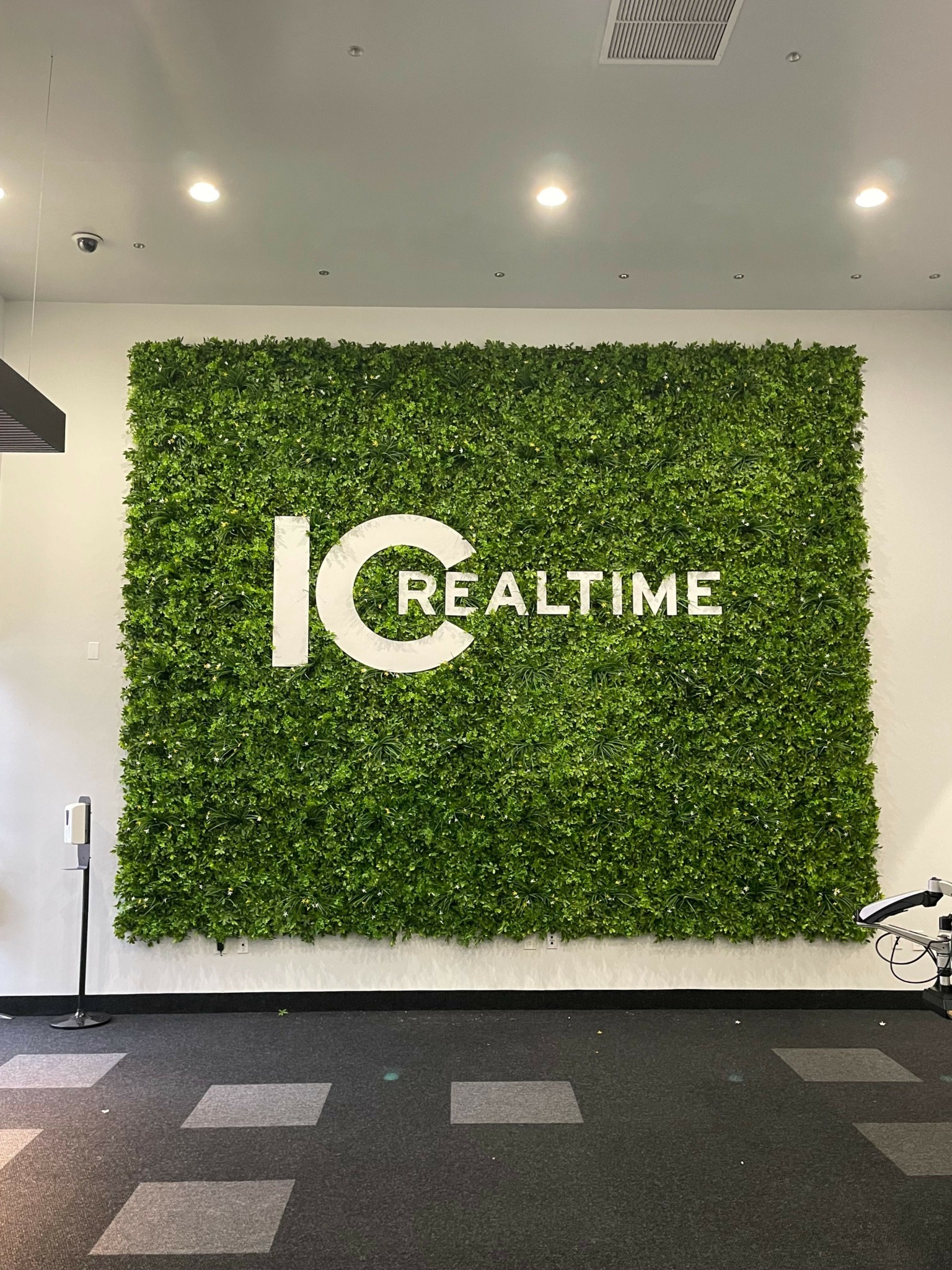 Green wall with white text and logo, adjacent to a parking lot with marked spaces.