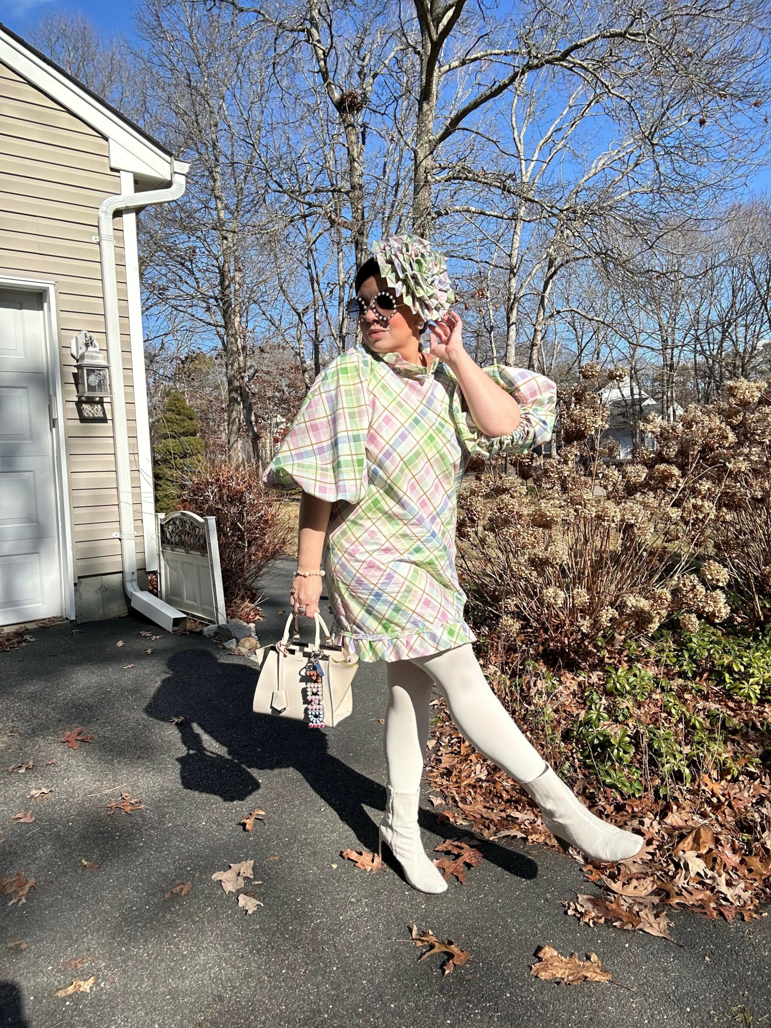 Person in plaid dress and headband standing on driveway with trees and house in background.