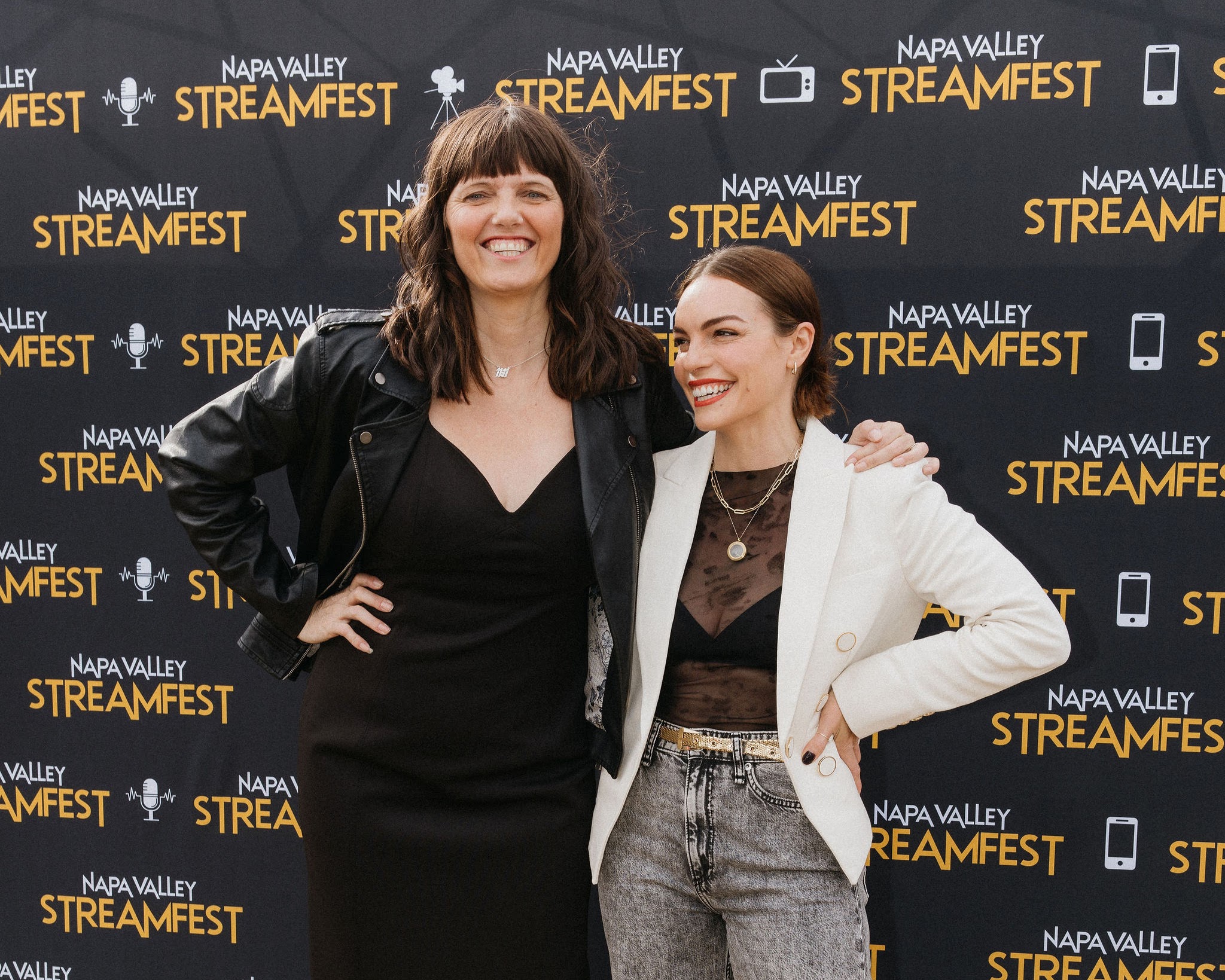 Two women smiling and posing together in front of a Napa Valley Streamfest backdrop.