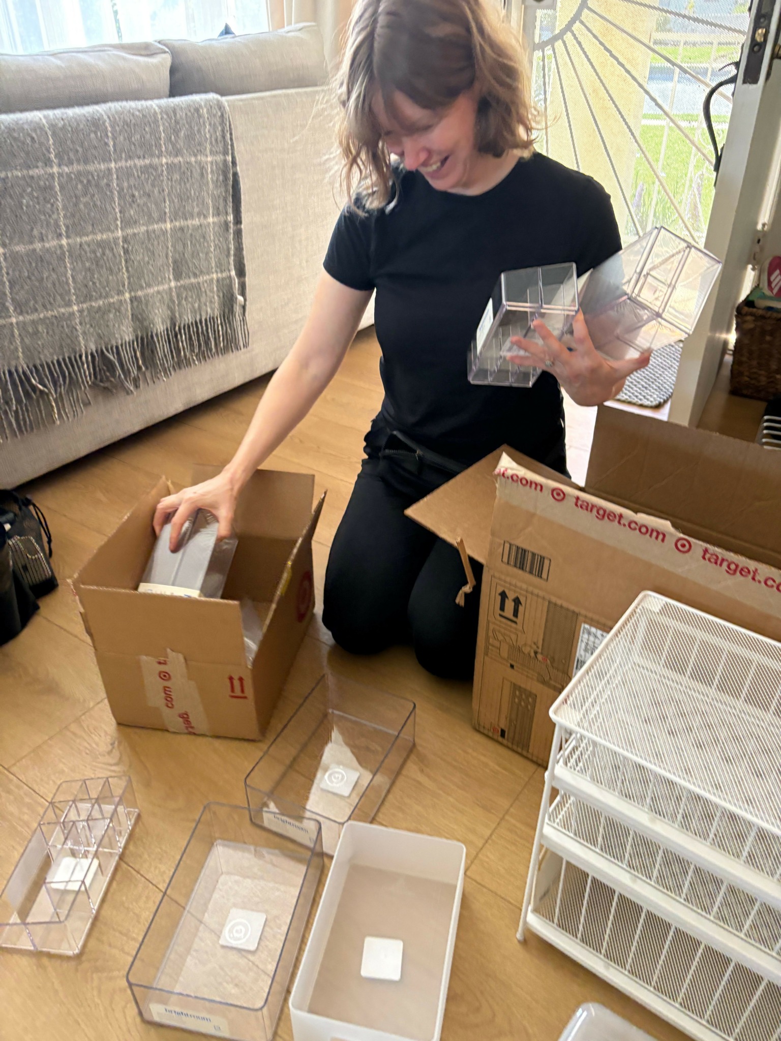 Child kneeling on floor, opening boxes with clear plastic containers, surrounded by packaging materials and storage racks.