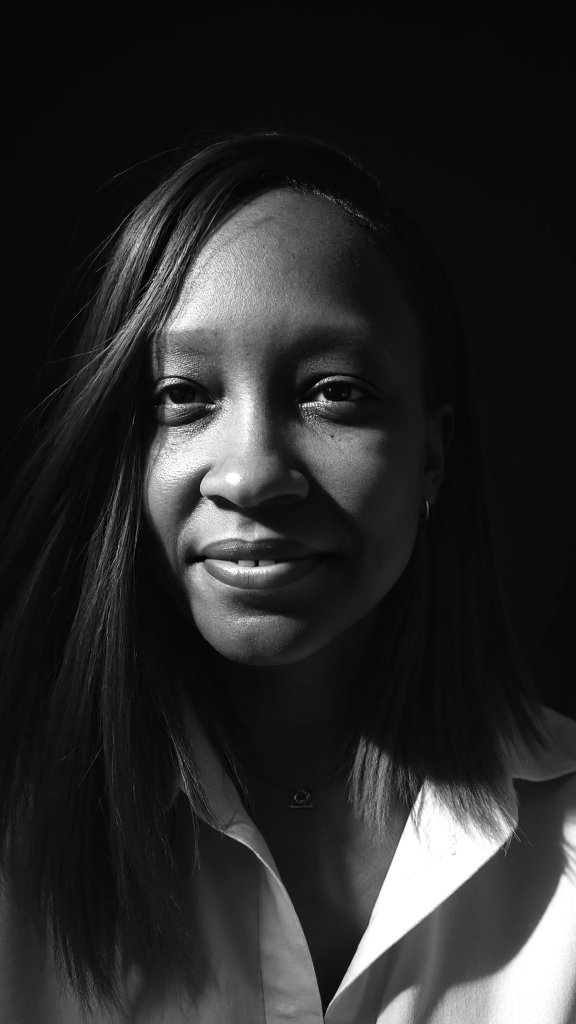 Portrait of a woman with long hair, smiling slightly, in black and white, with a dark background.
