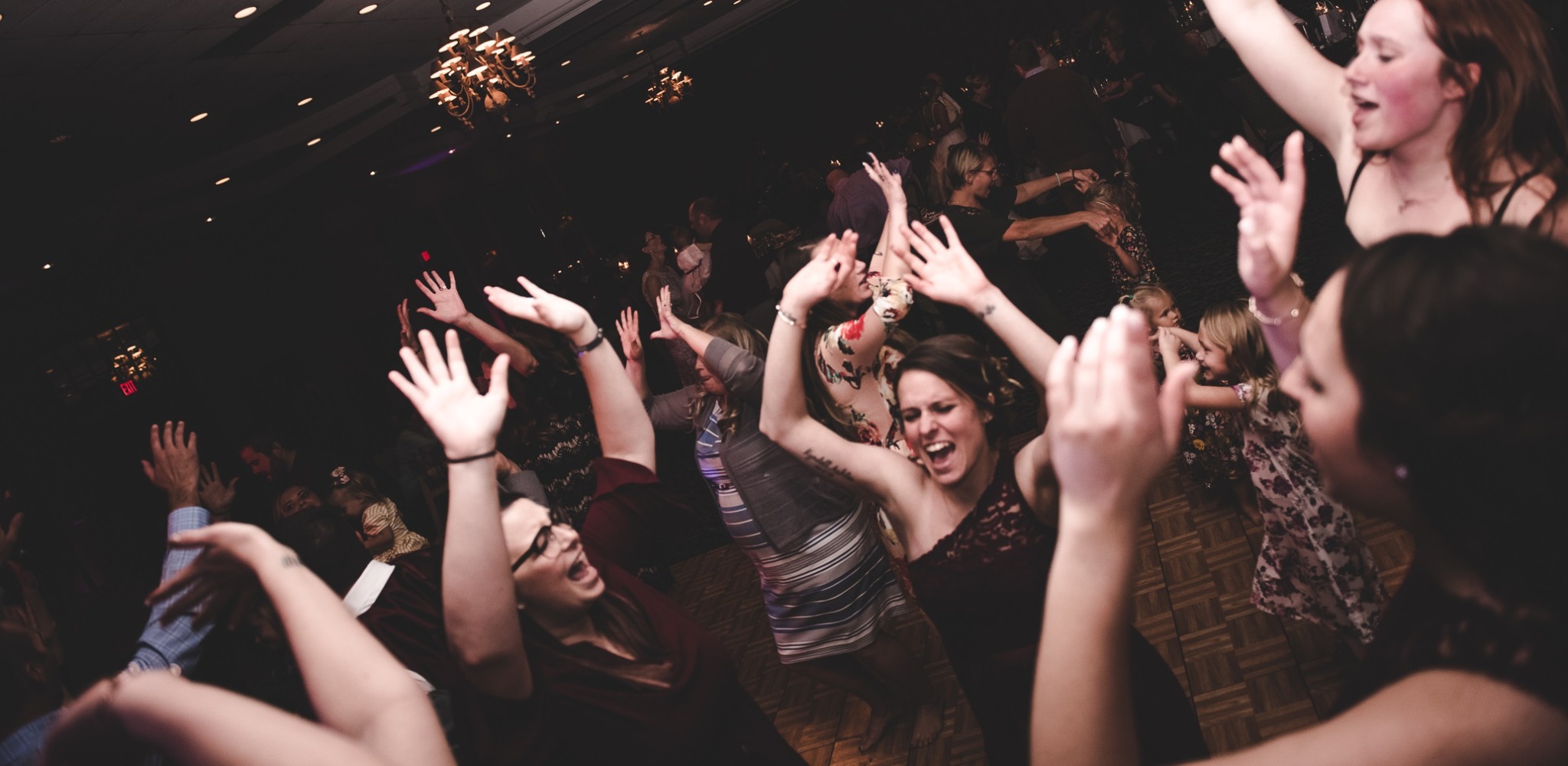 People dancing and raising hands at a party or celebration in a dark indoor setting.