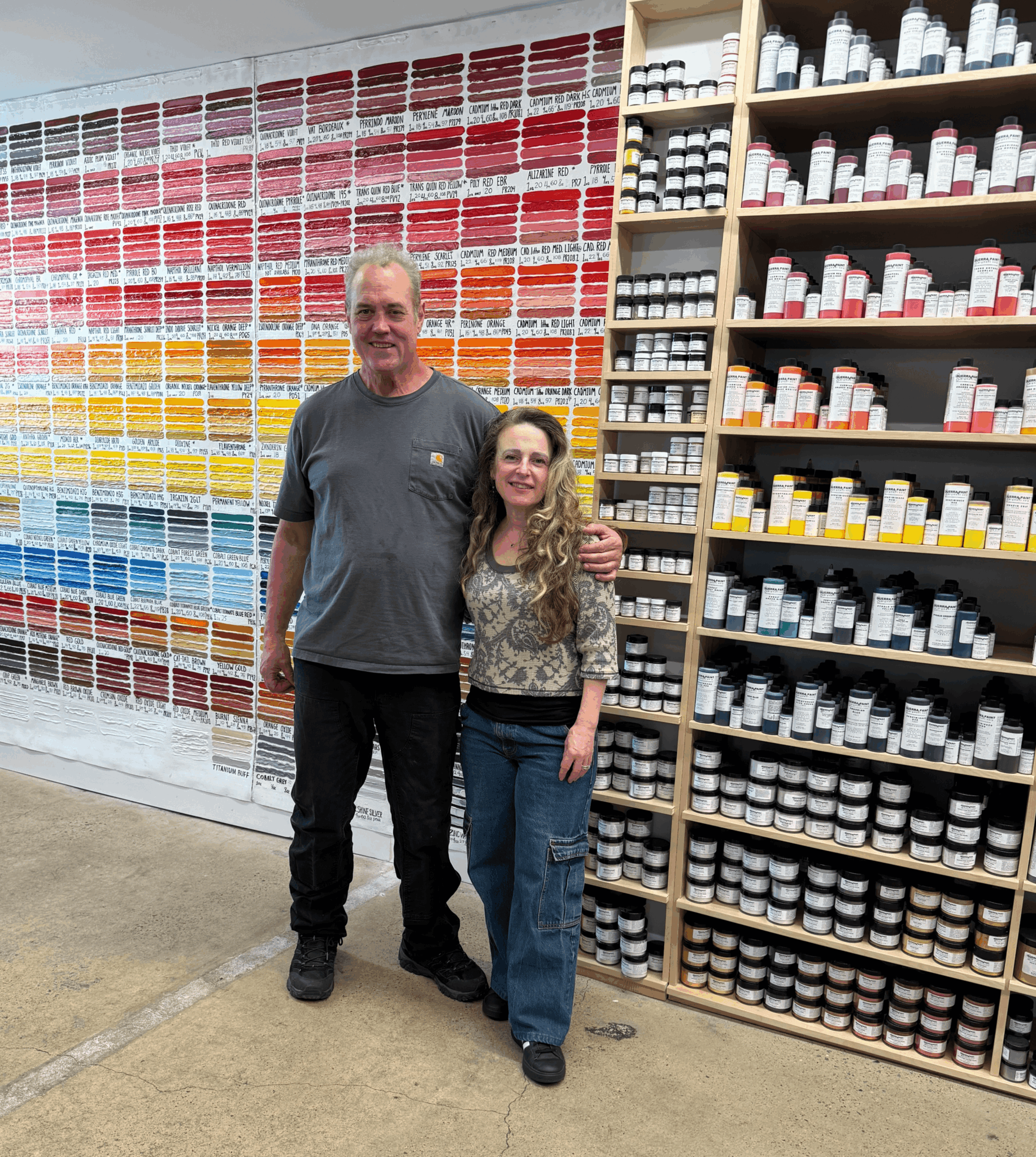 Two people standing in front of shelves filled with colorful paint samples and white paint bottles.