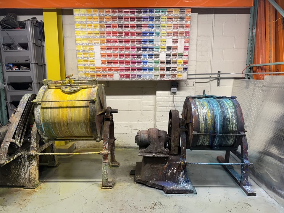 Two large industrial spools with yellow and blue materials, positioned on metal stands in a workshop setting.