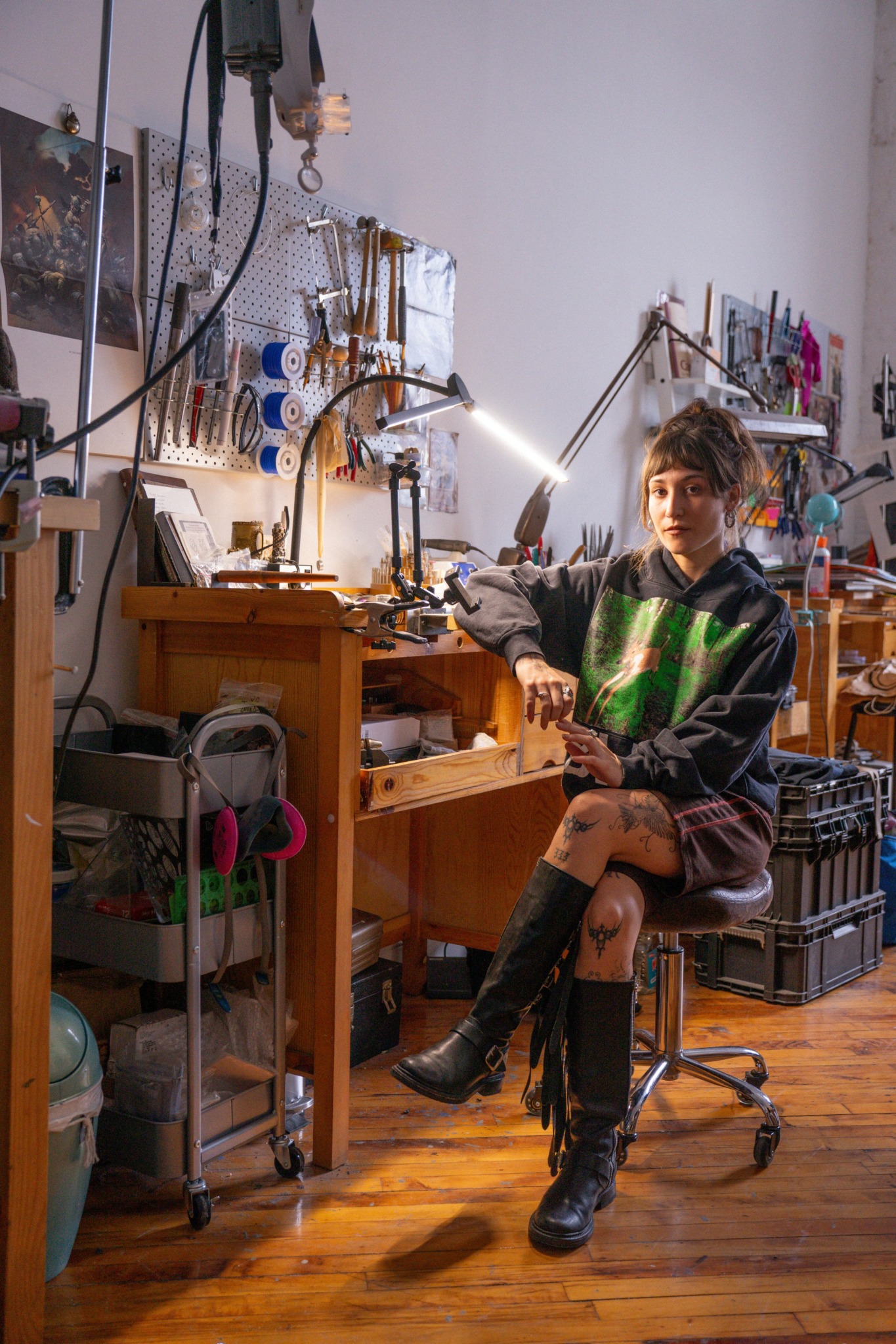 Young person sitting at a workbench in a workshop, surrounded by tools and equipment, with a focused expression.