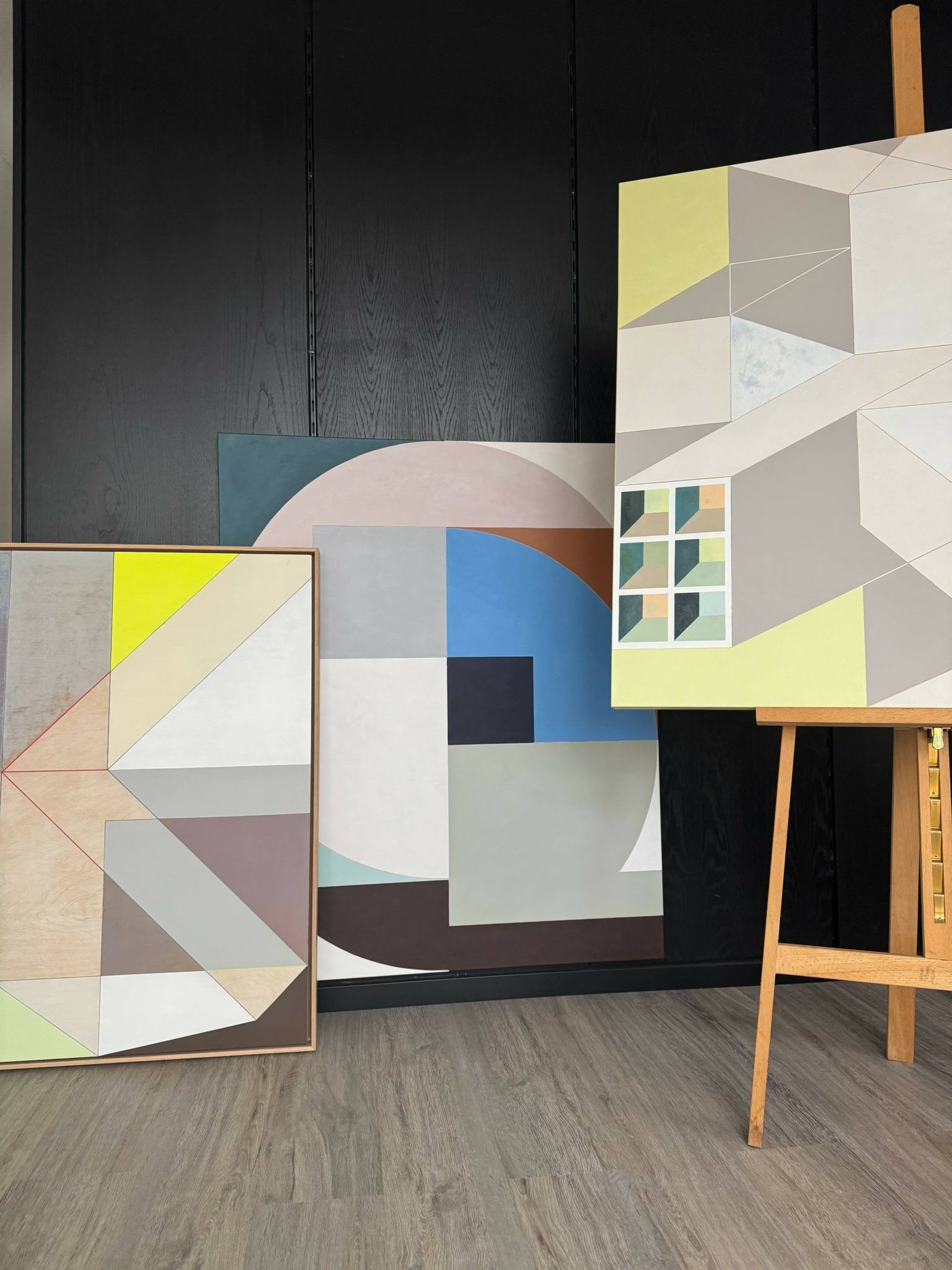 Two abstract geometric paintings on display, one on an easel, with a dark wall background.