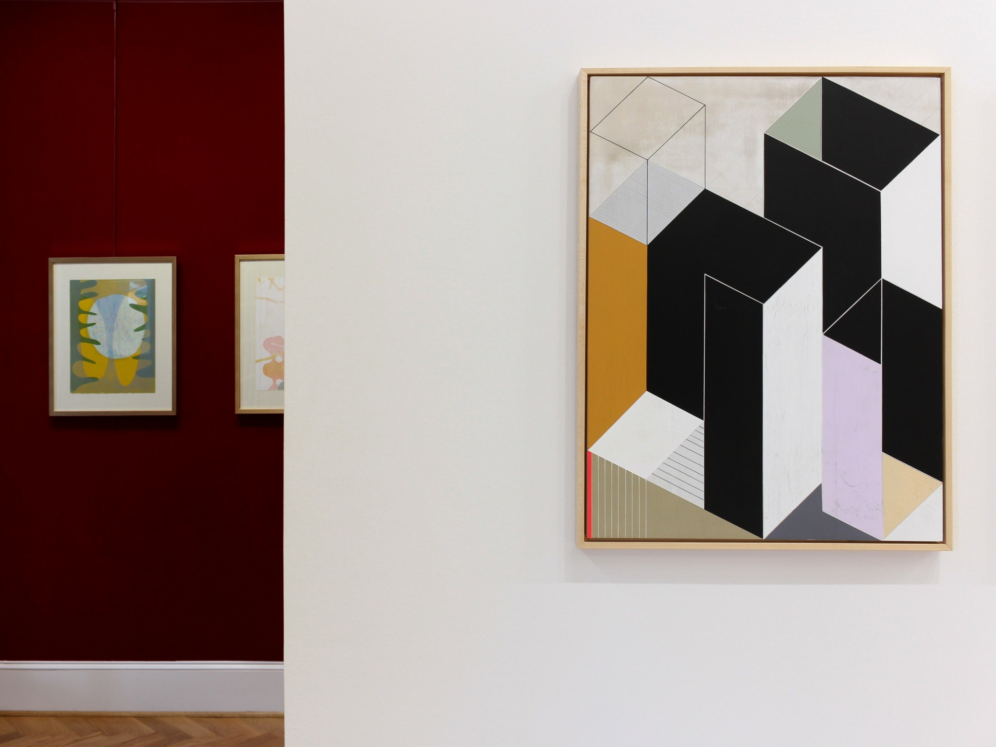 Gallery wall with abstract geometric art on a white wall, and two smaller framed artworks on a red wall.