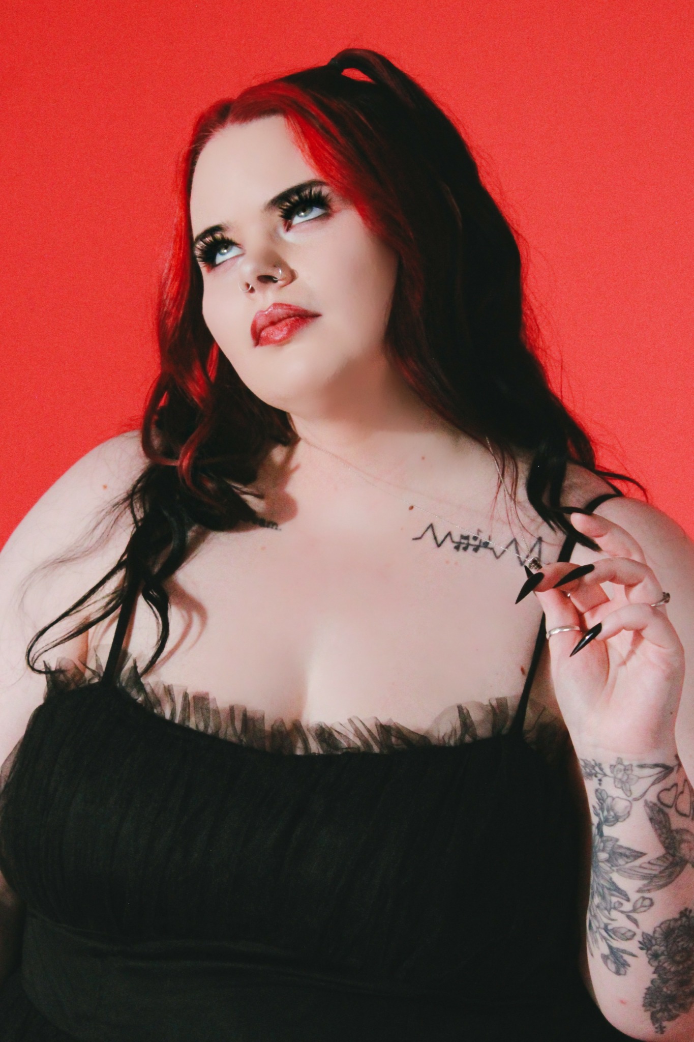 Woman with long dark hair and makeup, wearing a black top, against a red background.