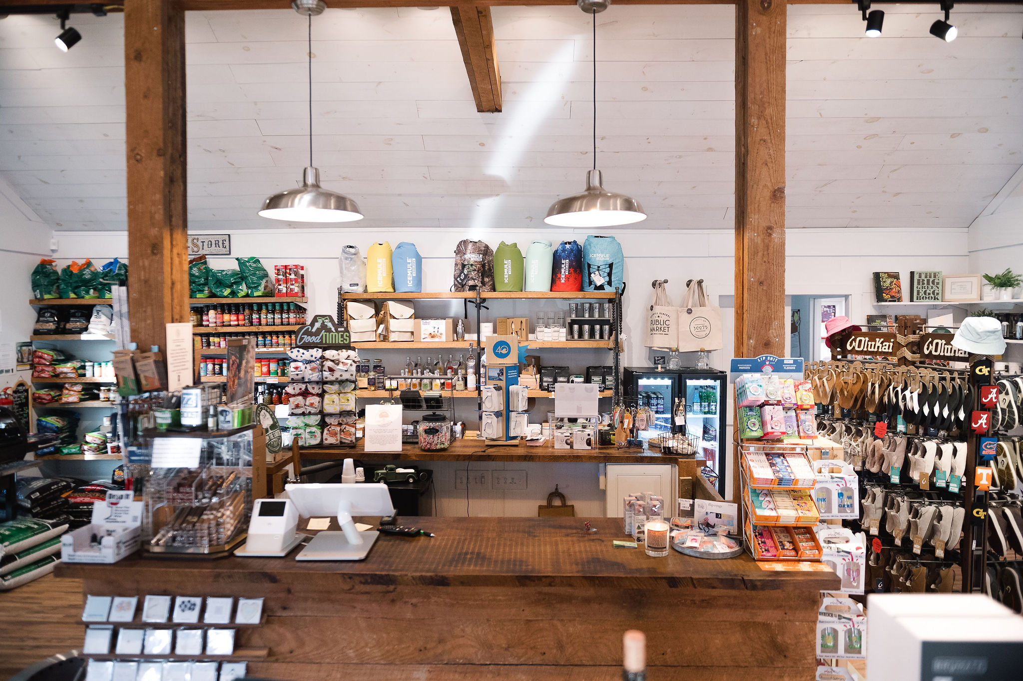 Interior of a store with shelves stocked with various products, a wooden counter, and overhead lighting.