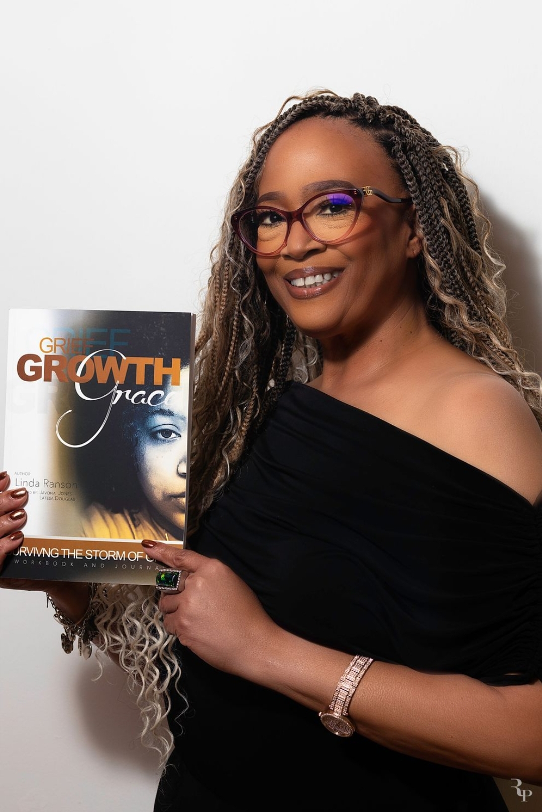 Woman with glasses and long curly hair holding a magazine with a woman's face on the cover.