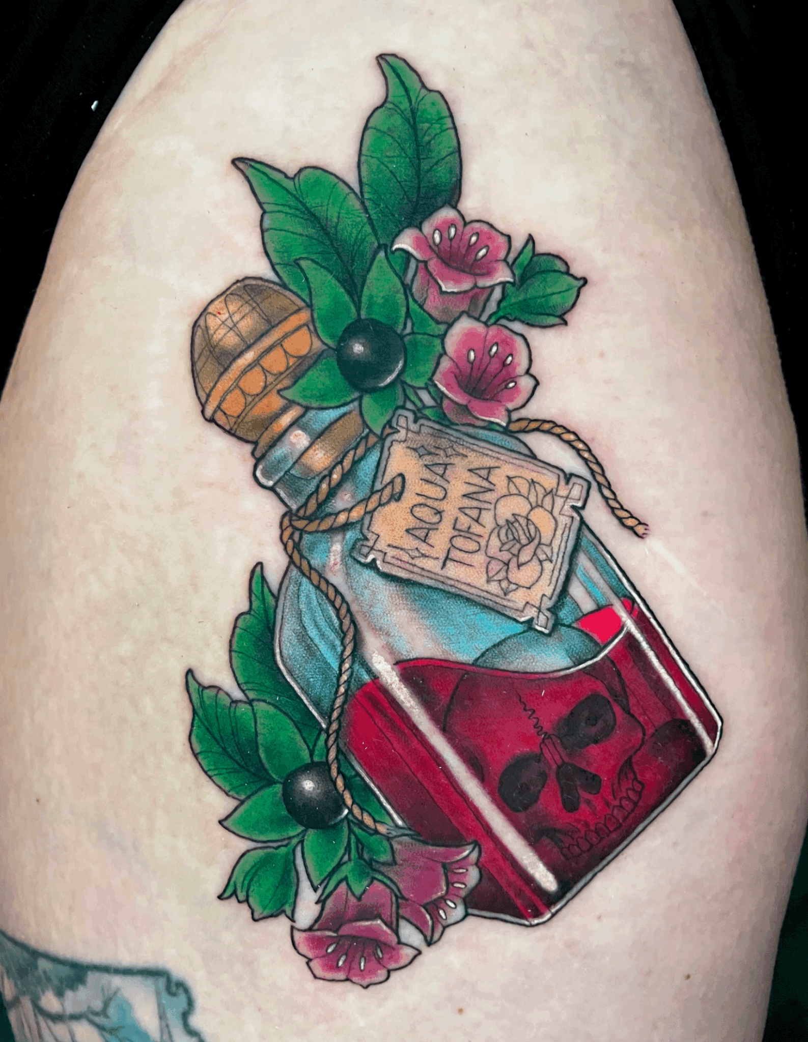 Tattoo of a bottle with skull, surrounded by pink flowers and green leaves.