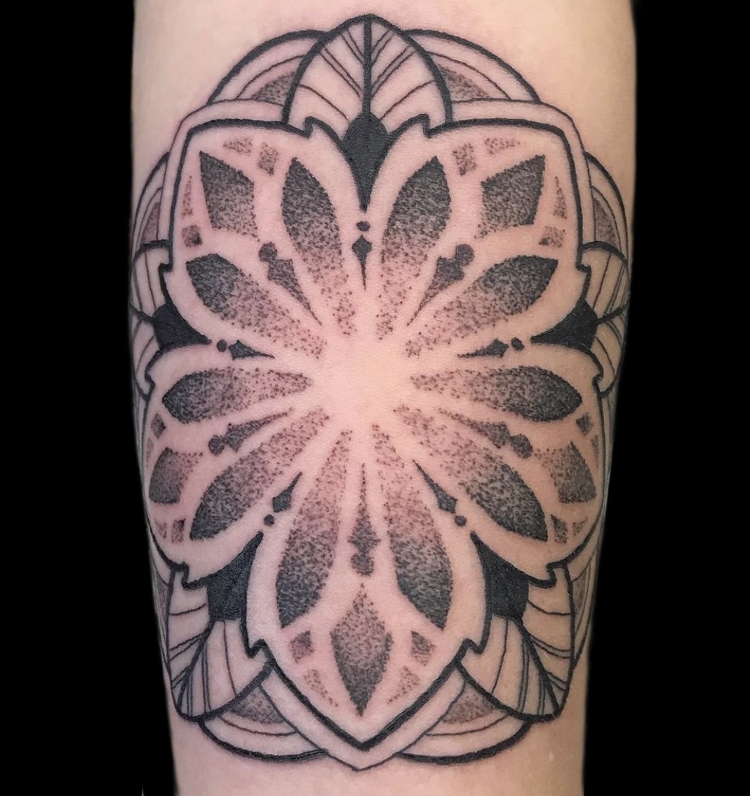 Black and gray floral tattoo with symmetrical petal patterns and geometric elements on skin.