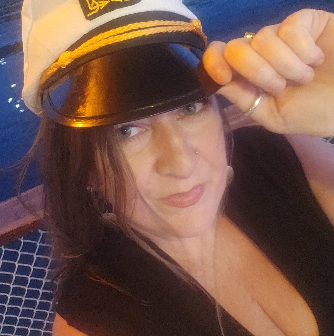 Woman wearing a captain's hat, adjusting it with her hand, with a blue background and a patterned surface.