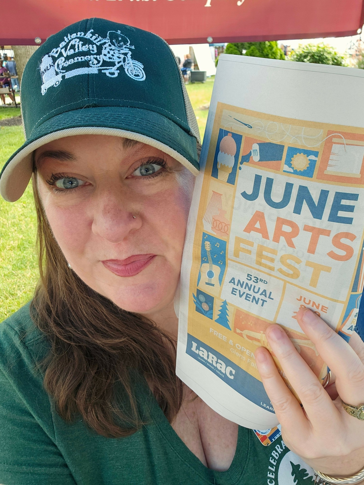Woman wearing a cap holding a colorful flyer outdoors, with trees and a building in the background.