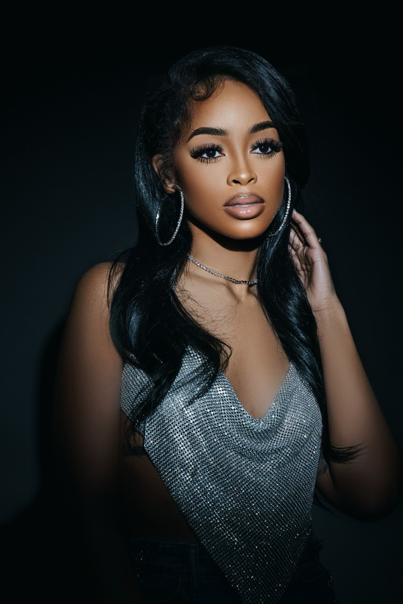 Young woman with long black hair, hoop earrings, and a silver top, posing against a dark background.