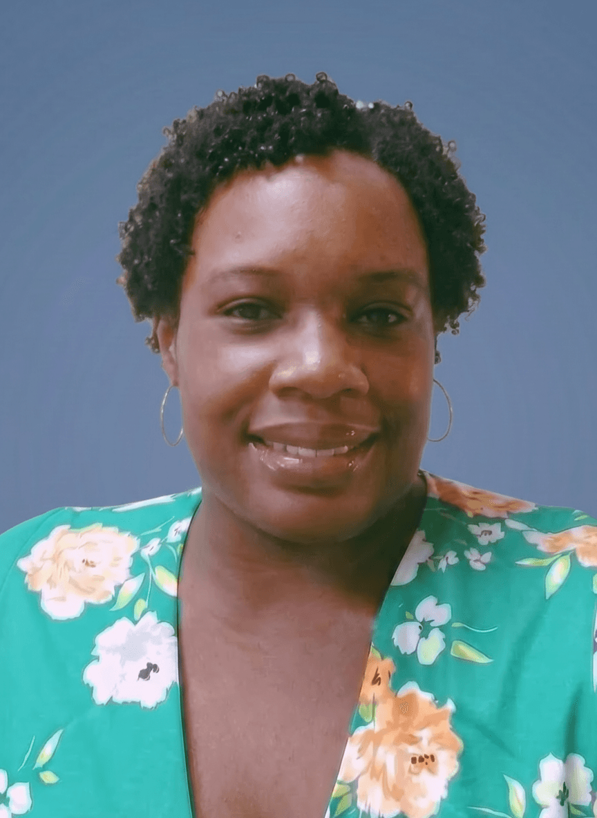 Woman with short curly hair smiling, wearing a floral top, against a blue background.