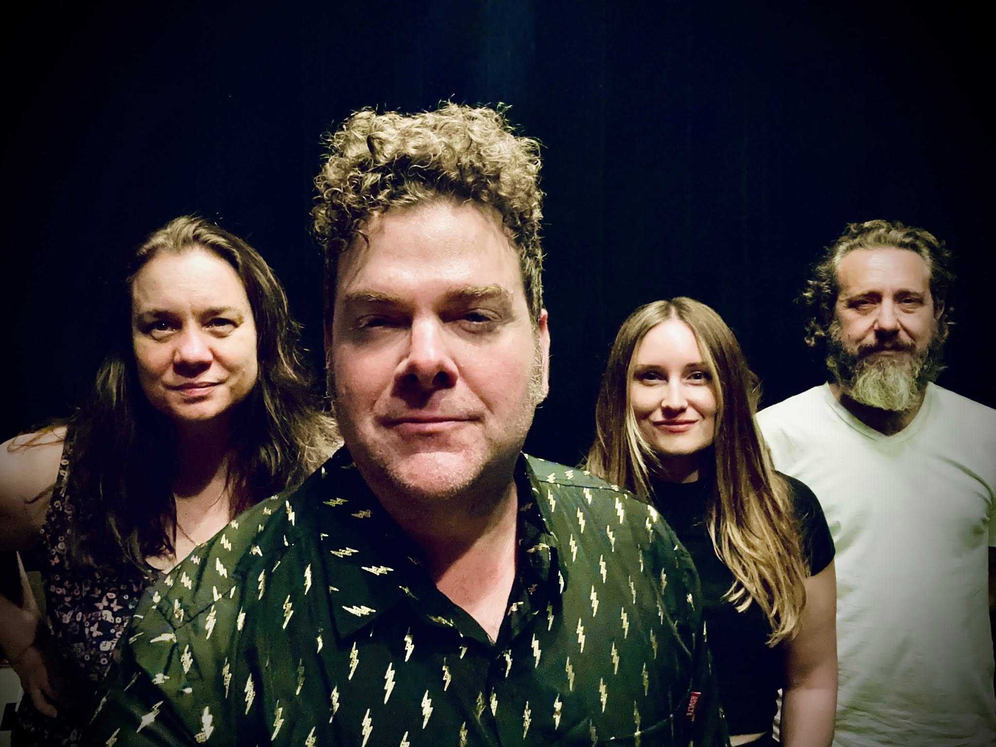Four people standing together, smiling, with a dark background.