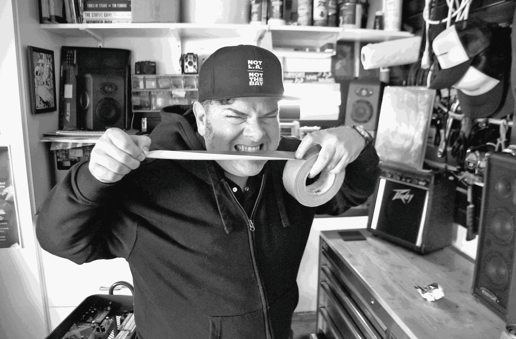 Person smiling and holding a tape measure in a room with electronic equipment and shelves.