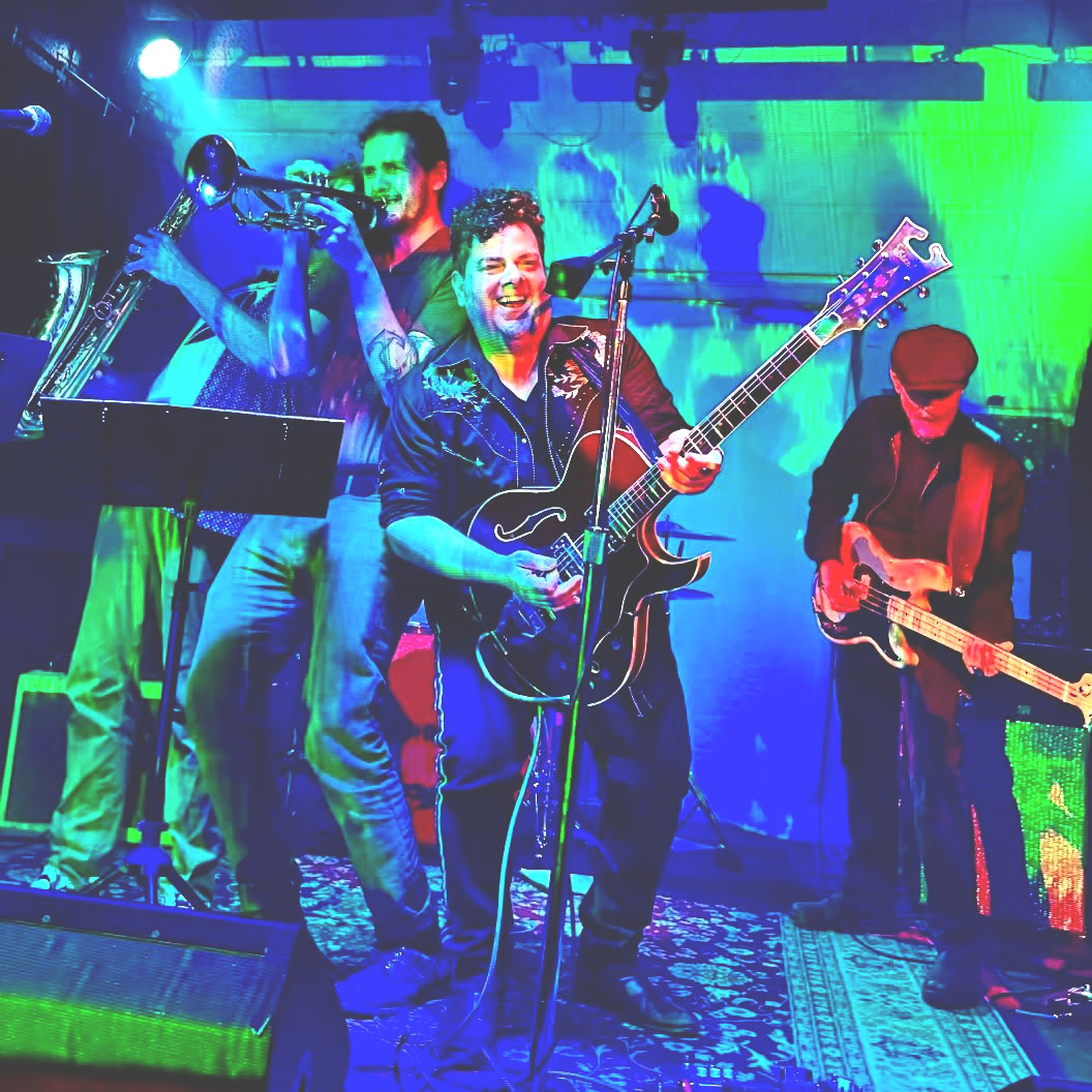 Band performing on stage with colorful lighting, featuring a guitarist, saxophonist, and other musicians.