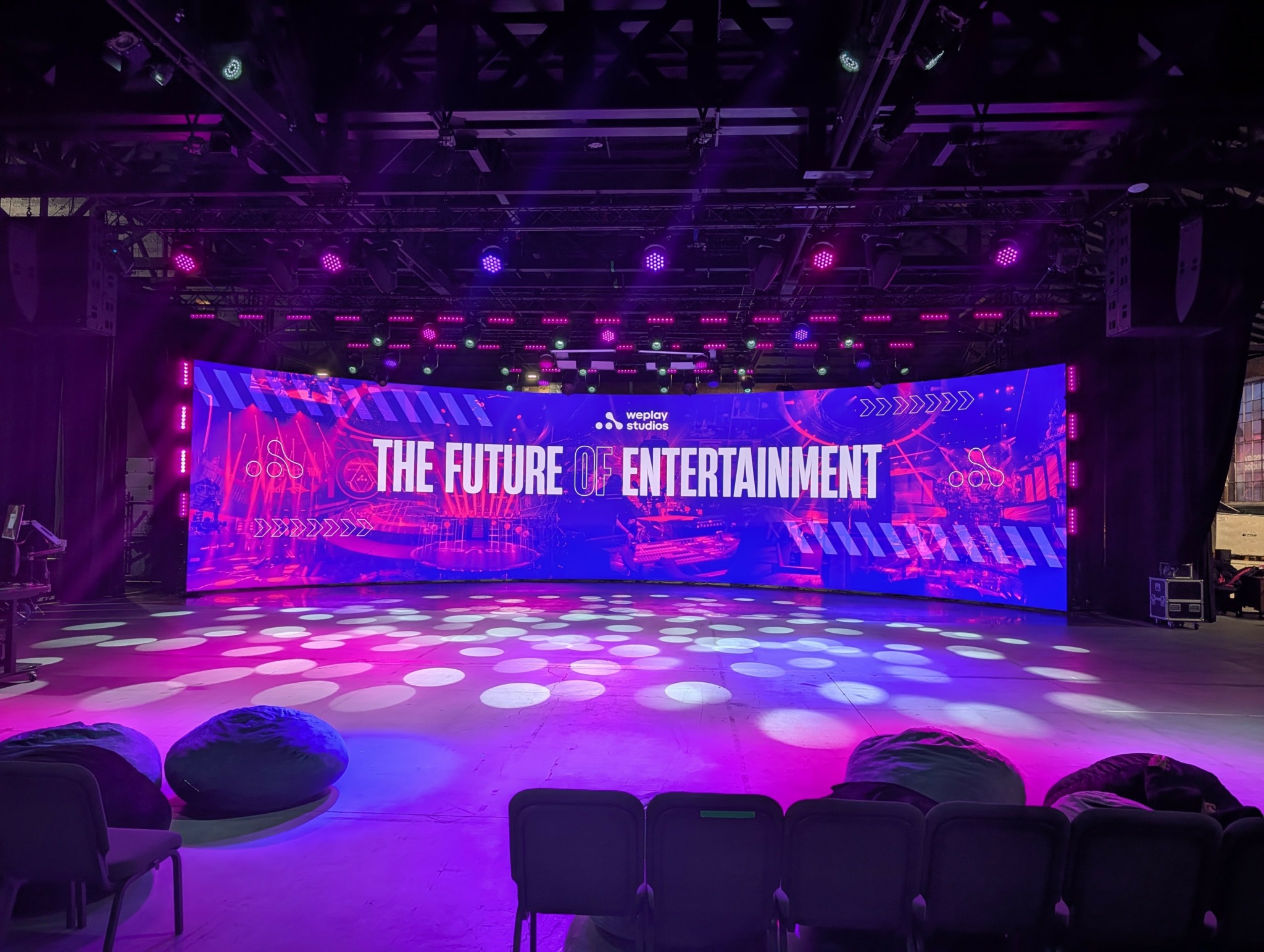 Stage with a large digital screen displaying 'The Future of Entertainment' in a dark, purple-lit venue.