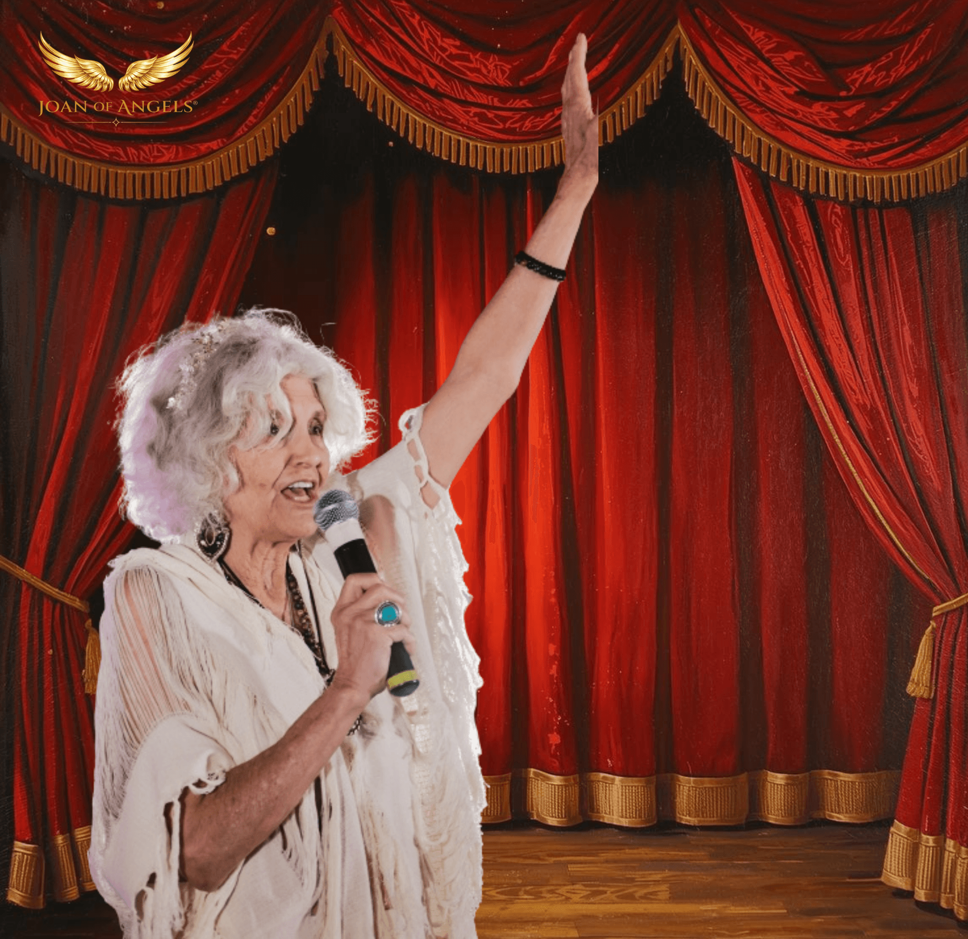 Older woman with curly white hair speaking into a microphone on stage with red curtains behind her.