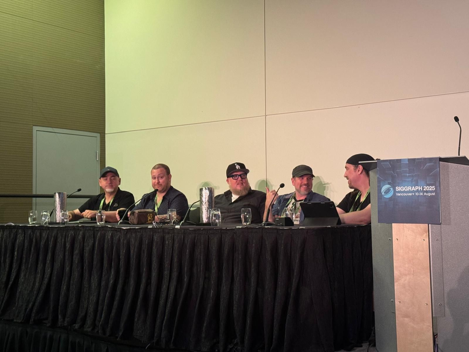 Five people seated at a long table on a stage with a podium and microphone, in a conference room.