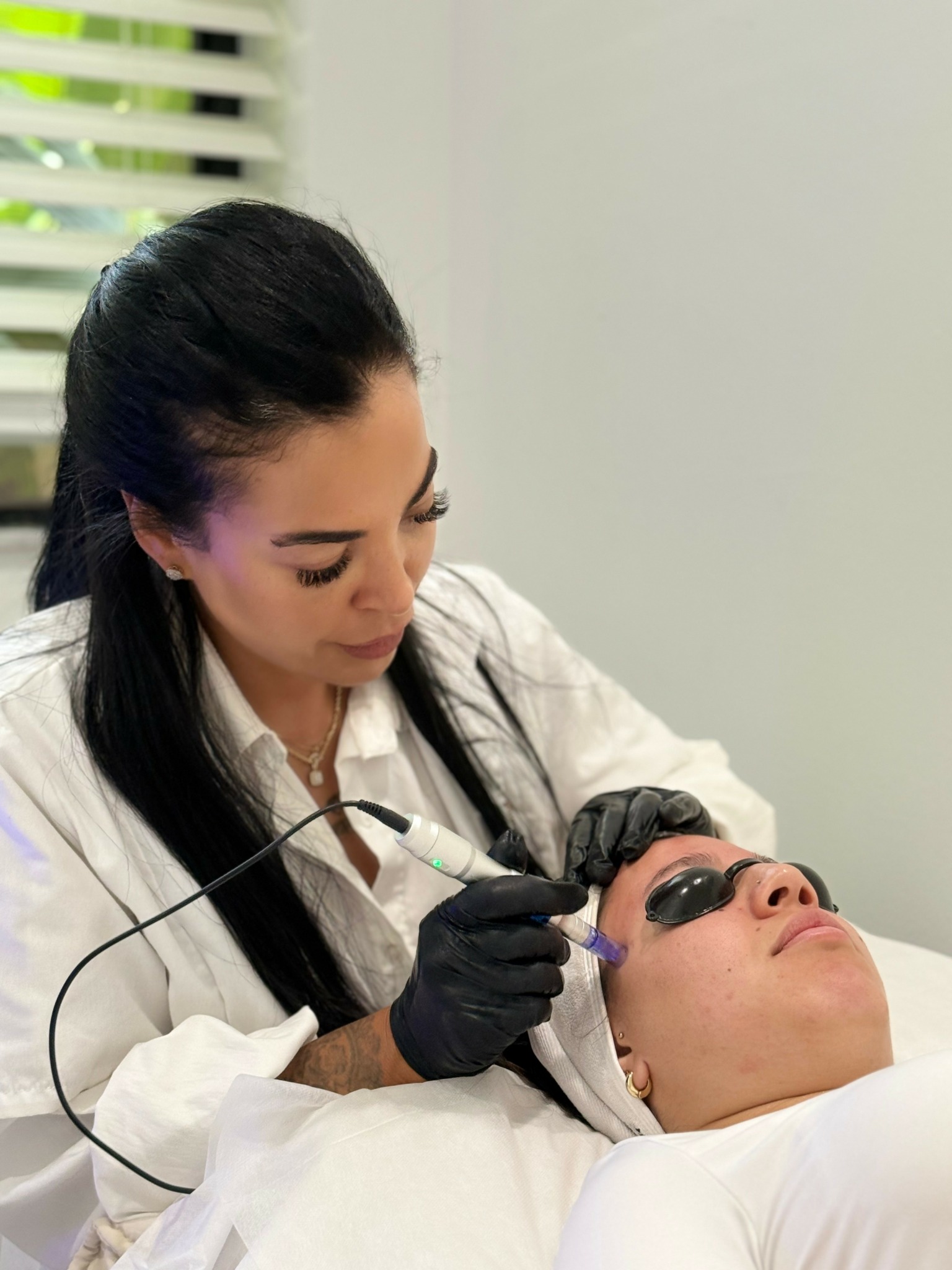 A woman in black gloves performs a cosmetic procedure on a person lying down with protective eyewear.