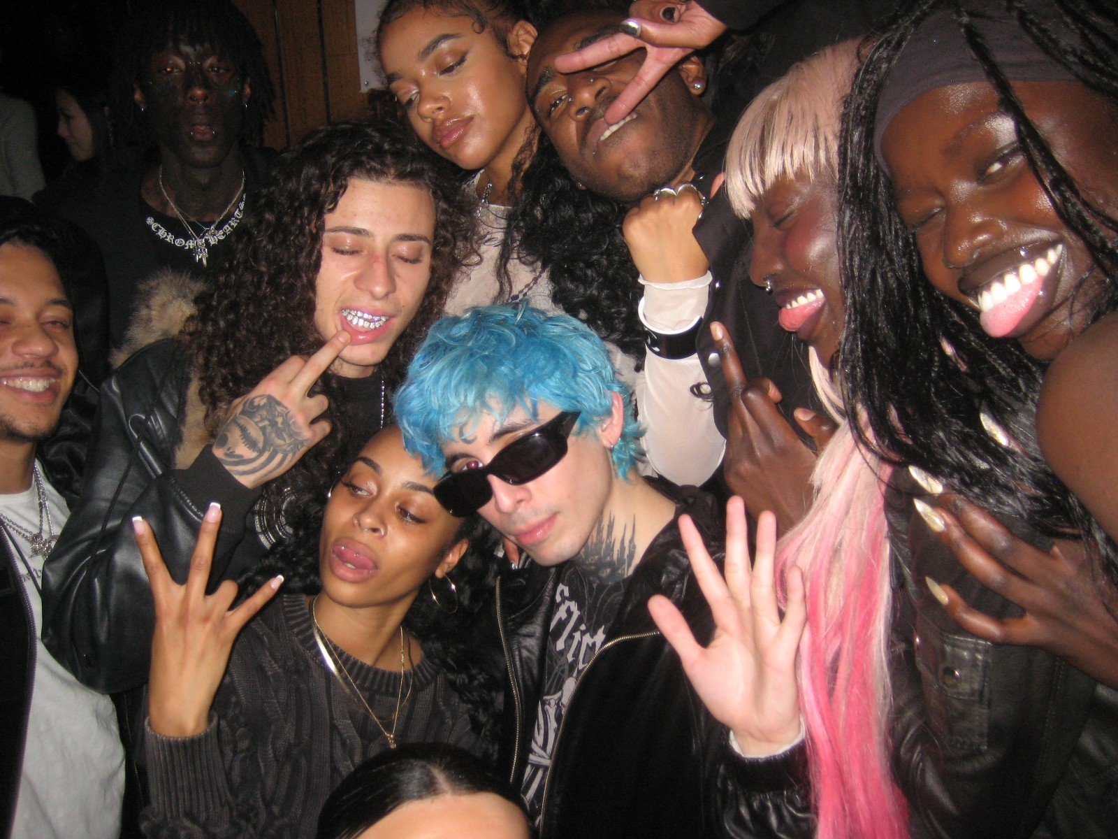 Group of diverse young people smiling, making hand gestures, and posing closely together indoors.
