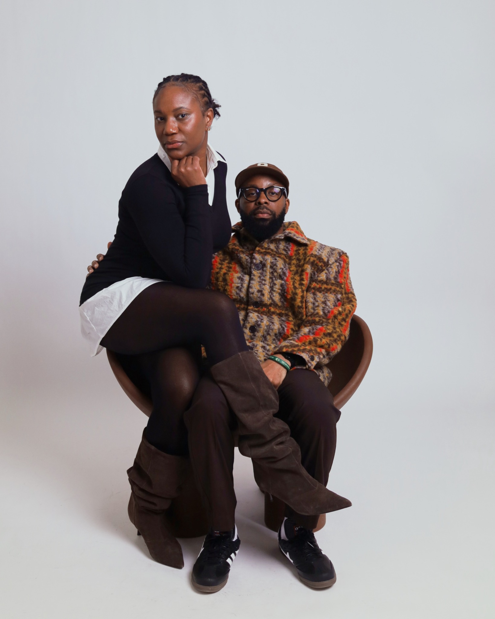 A woman sits on a man's lap, both facing forward, against a plain light background.