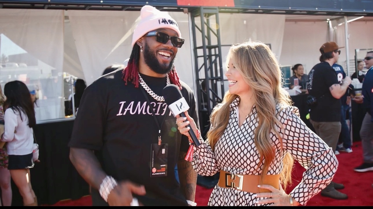 Man with sunglasses and a woman with a microphone talking at an outdoor event.
