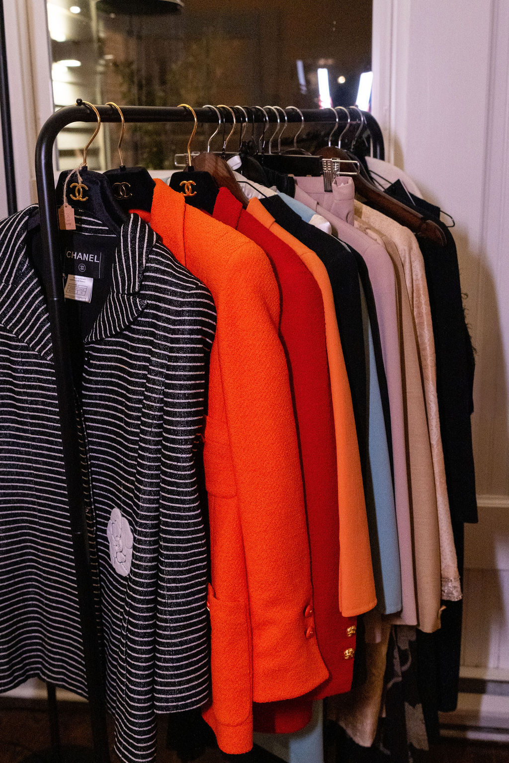 Clothing rack with striped, orange, black, beige, and light-colored shirts and jackets hanging on hangers.