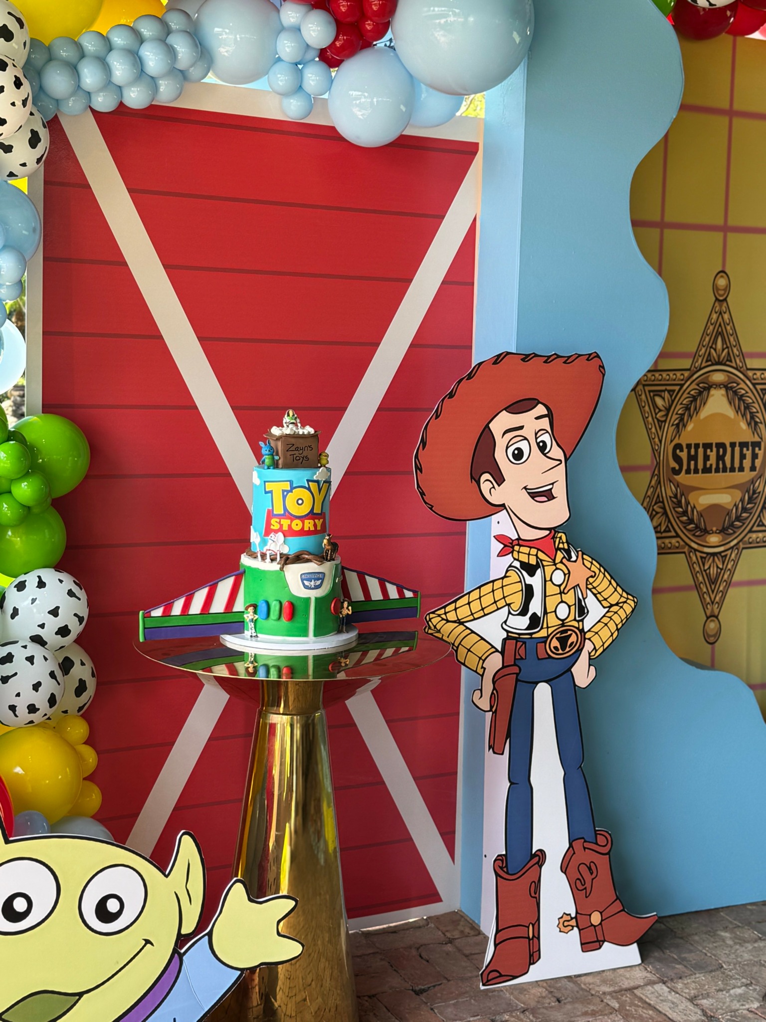 Decorative display with Toy Story theme, including a cake, a cardboard Woody figure, and colorful balloons.