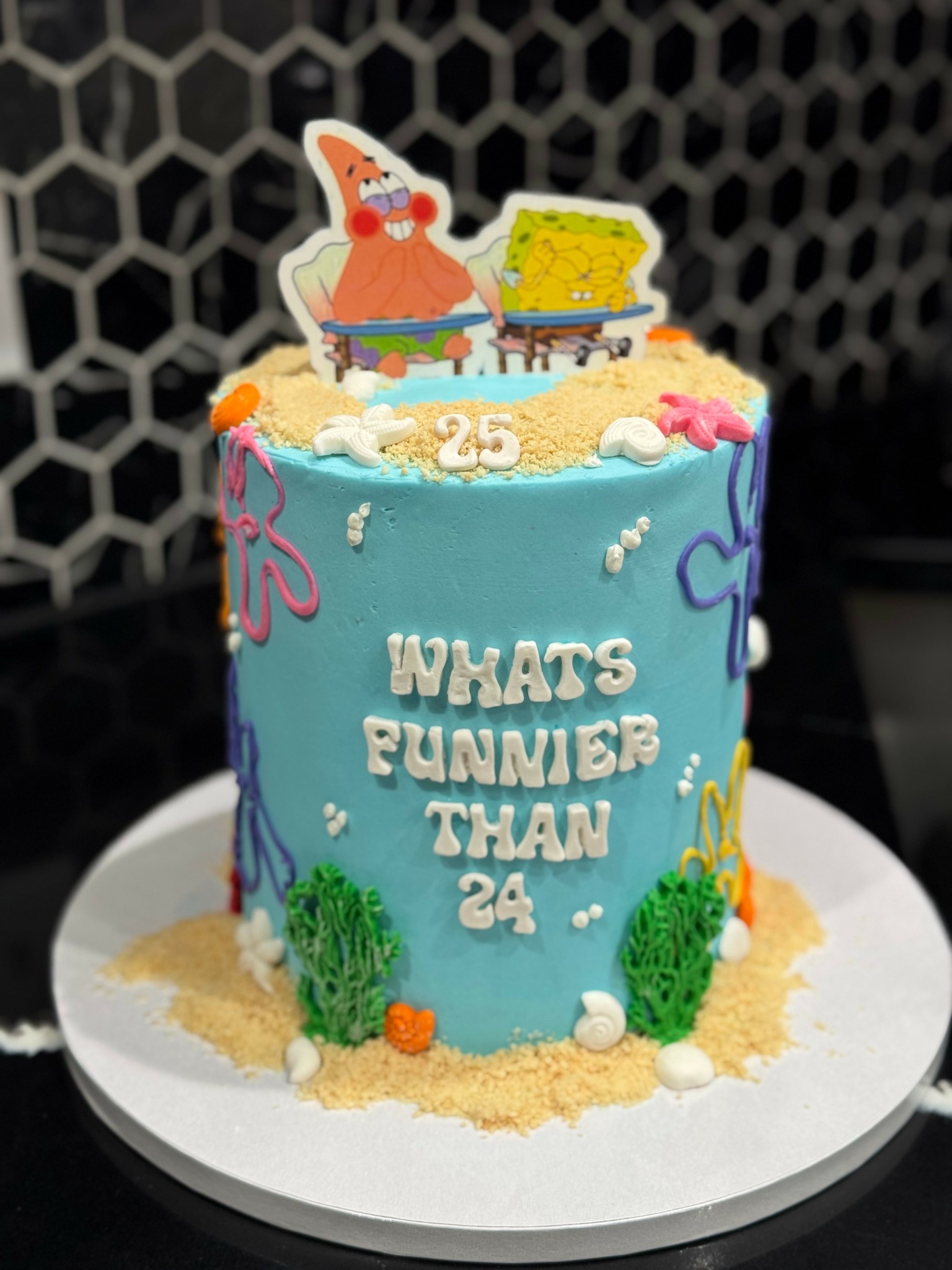 Colorful birthday cake with SpongeBob and Patrick toppers, blue frosting, and decorative elements, celebrating 24th birthday.