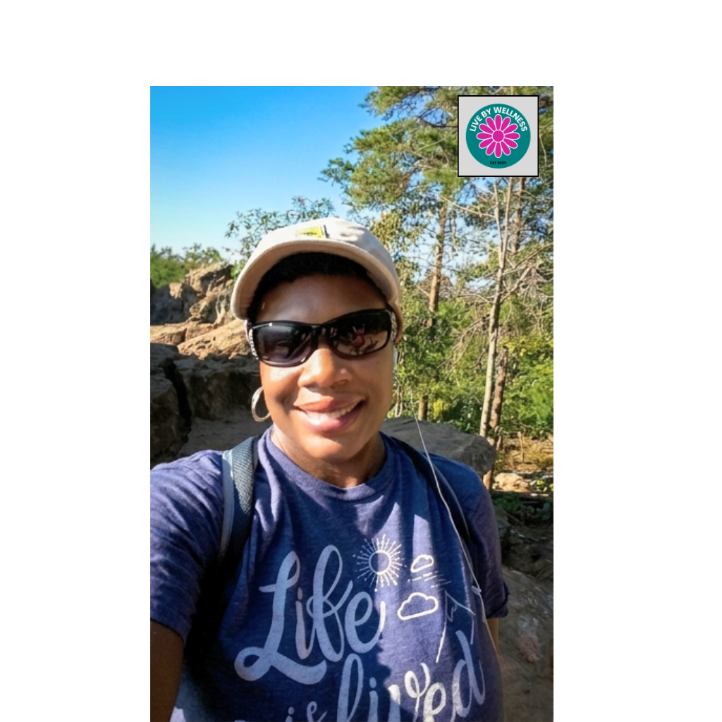 Person outdoors wearing sunglasses, hat, and a blue shirt with white text, smiling, with trees and a sign in background.