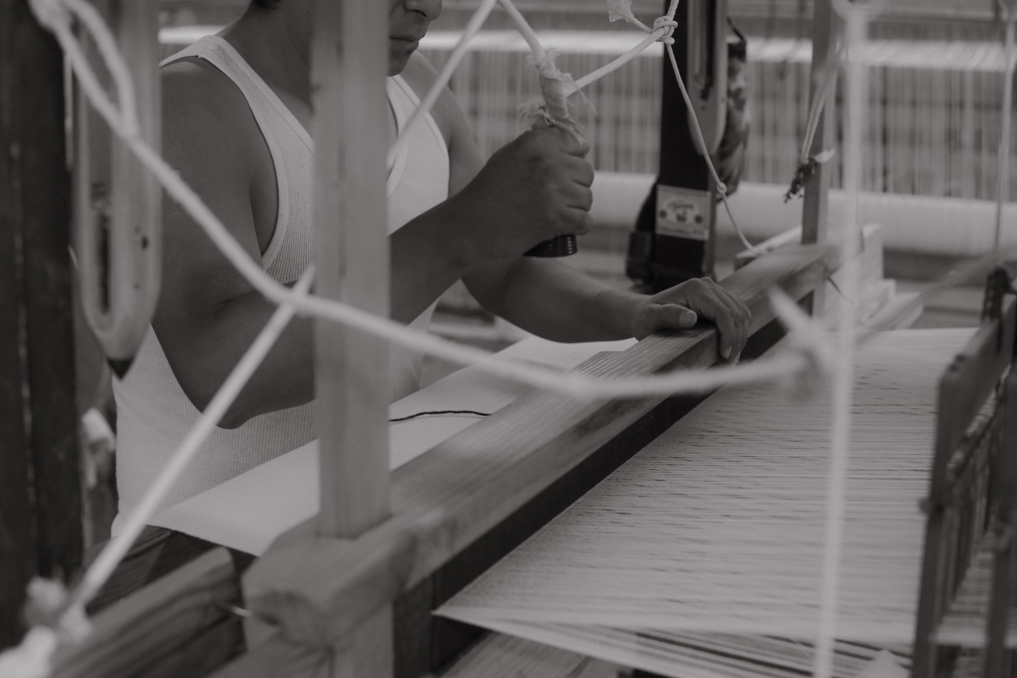 Person working at a desk with papers and a pen, surrounded by ropes or strings, in black and white.