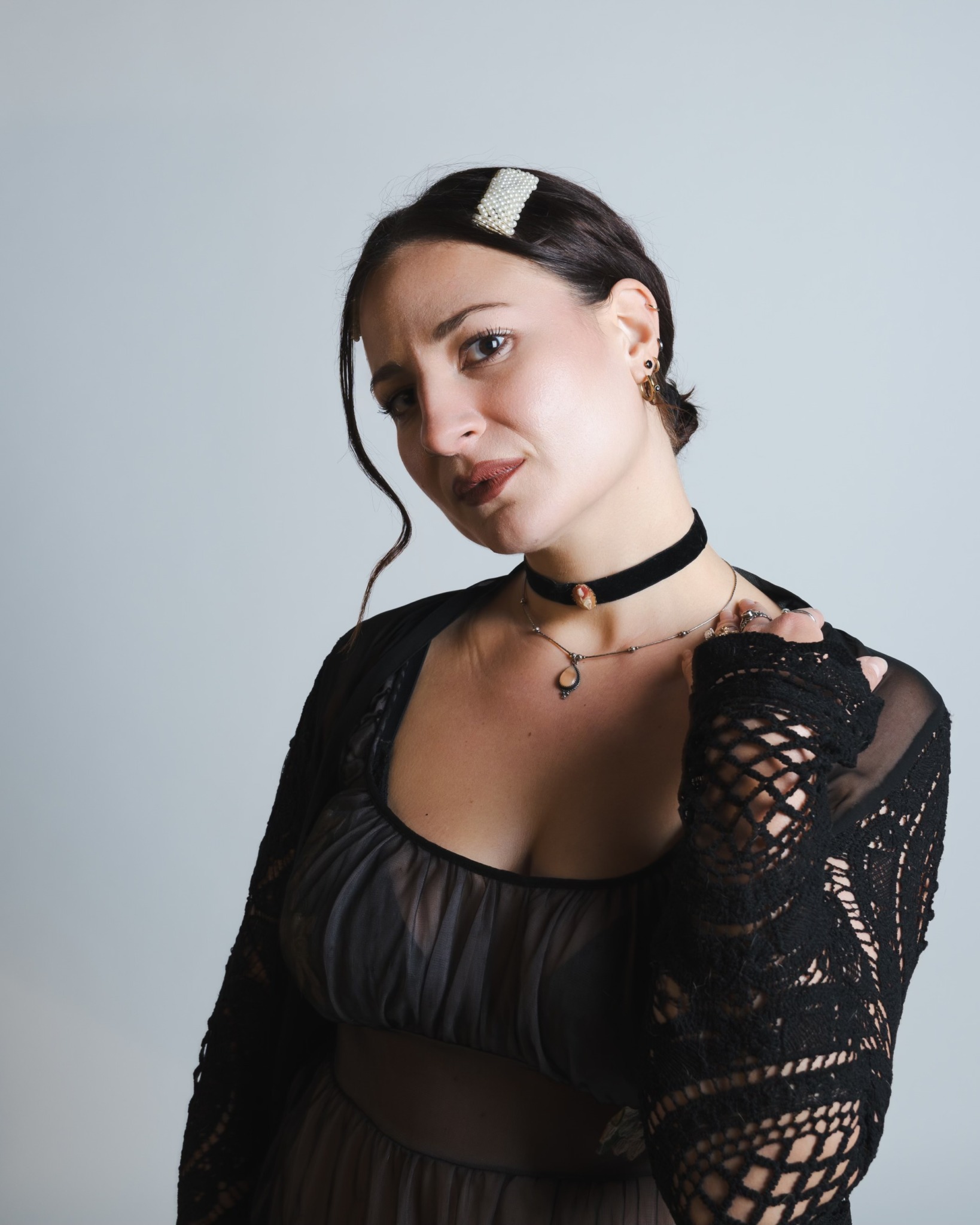 Young woman with dark hair, wearing a black lace top and choker, looking at the camera.