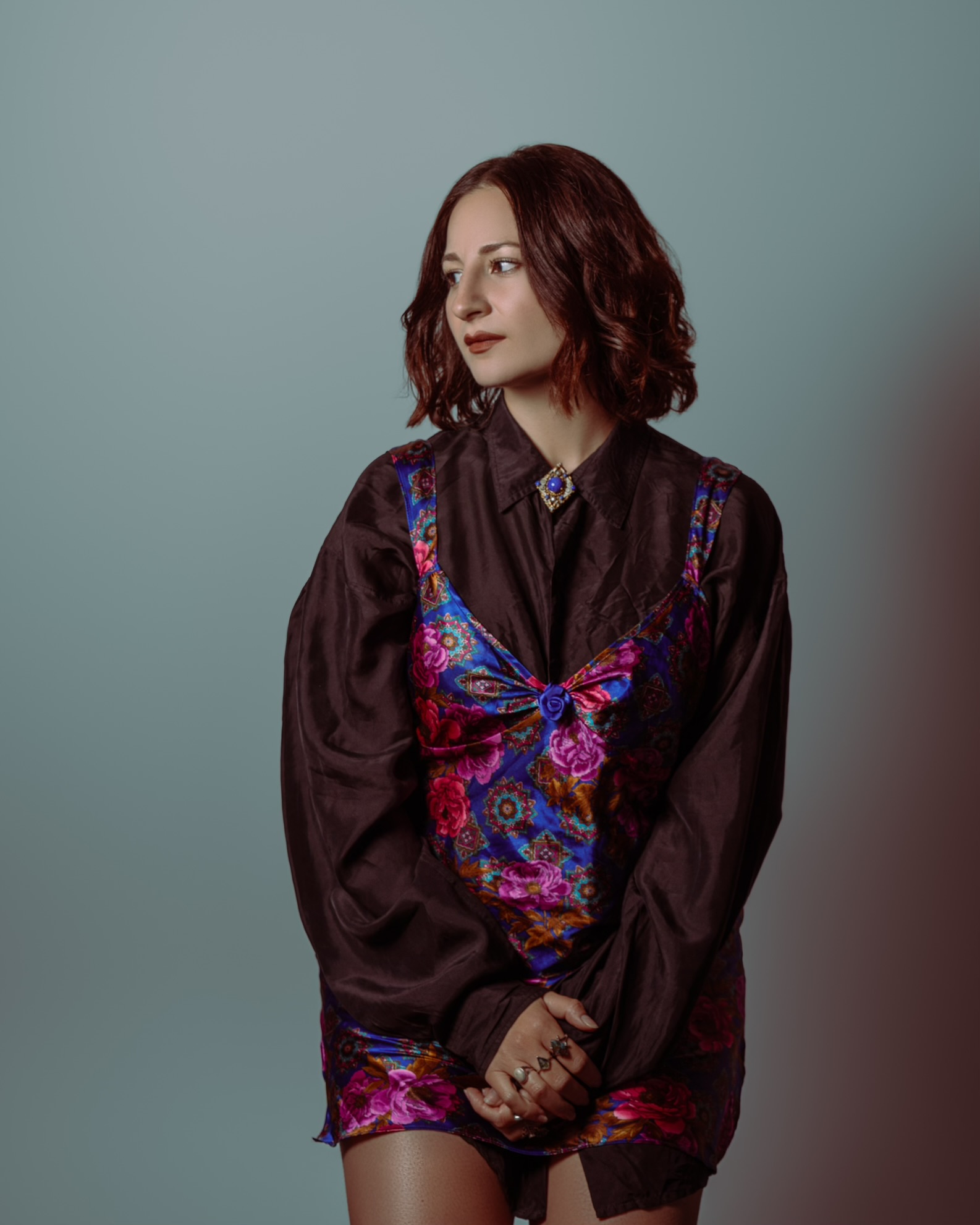 Woman with shoulder-length wavy hair wearing a dark blouse with colorful butterfly embroidery, standing against a plain background.