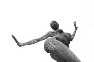 A person with textured skin poses with arms outstretched and head tilted back against a white background.