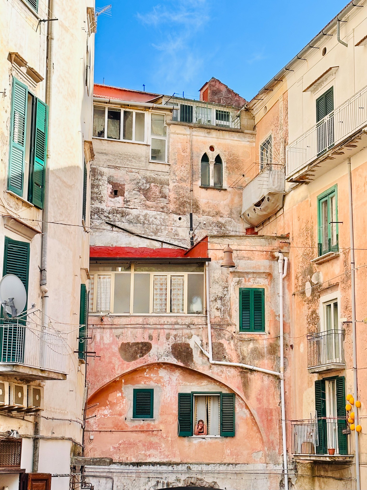 Multiple old buildings with windows, balconies, and weathered walls under a blue sky.