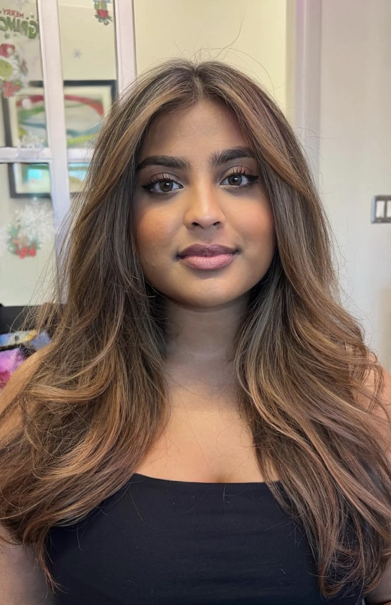 Young woman with long, wavy hair and makeup, wearing a black top, indoors with colorful background.