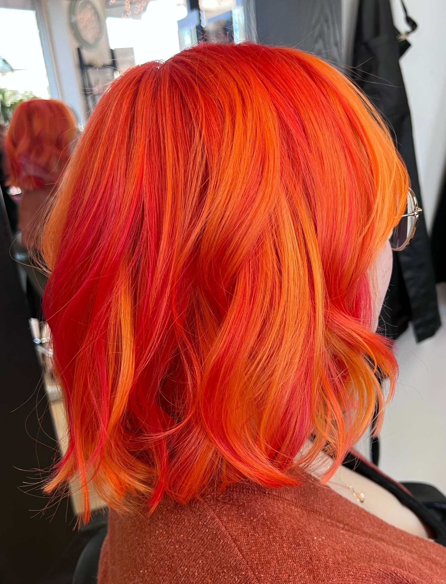 Side view of a person with vibrant red and orange wavy hair in a salon.
