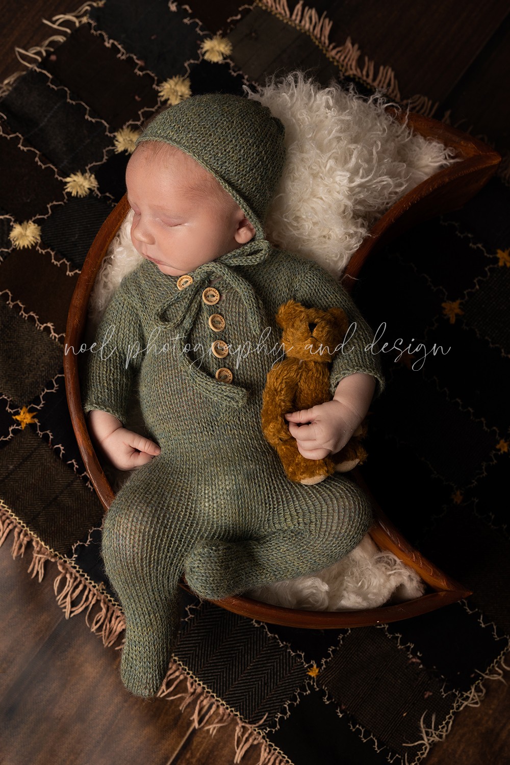 Baby in green knit outfit and hat sleeping on a blanket with a teddy bear.