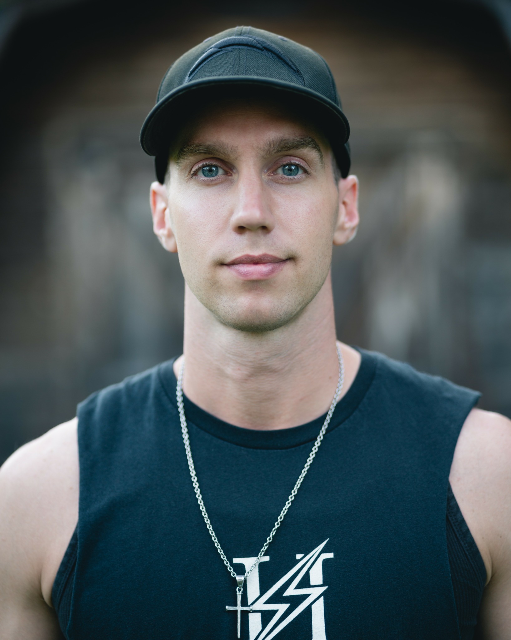 Young man wearing a black cap and sleeveless shirt, looking at the camera outdoors.